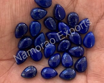 May include: A collection of deep blue, teardrop-shaped lapis lazuli gemstones. The polished stones have a smooth, reflective surface with flecks of gold. The gemstones are displayed in a hand.