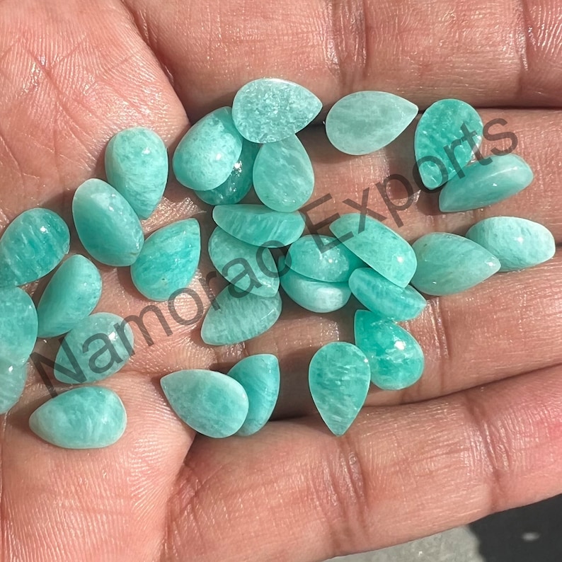 May include: A collection of teal green pear-shaped gemstones, also known as Amazonite, in various sizes. The gemstones are smooth and polished, with a translucent appearance.