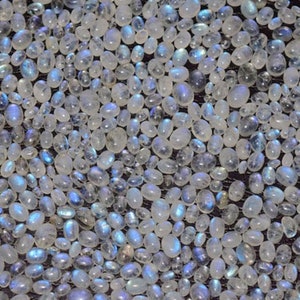 May include: A close-up view of a large quantity of white moonstone chips. The stones are smooth and oval-shaped, with a slight iridescent sheen.