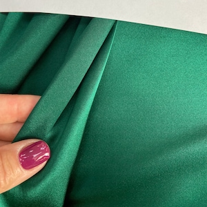 Könnte beinhalten: Nahaufnahme eines tiefgrünen Satin-Stoffes mit einer glatten, seidenartigen Textur. Der Stoff ist gefaltet und drapiert, wodurch weiche Falten und Kurven entstehen.
