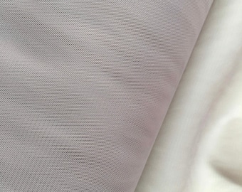 May include: Close-up of two fabric samples. One is a light gray, textured mesh fabric, and the other is a smooth, off-white fabric. The fabrics are folded, revealing their different textures and colors. Ideal for textile projects.