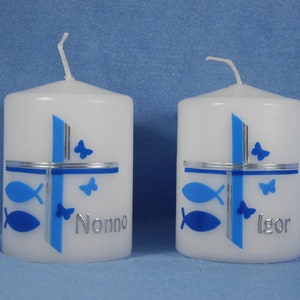K&ouml;nnte beinhalten: Zwei wei&szlig;e Kerzen mit blauen und silbernen Designs. Die Kerzen haben ein Kreuz mit Fischen und Schmetterlingen. Eine Kerze sagt "Nonno" und die andere sagt "Igor".
