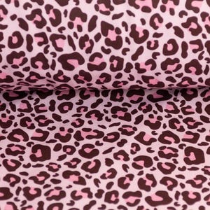 Könnte beinhalten: Rosa Stoff mit einem braunen und rosa Leopardenmuster. Der Stoff ist gefaltet, wodurch das Muster sichtbar wird. Die Leopardenflecken variieren in Größe und Form und erzeugen ein dynamisches Design.