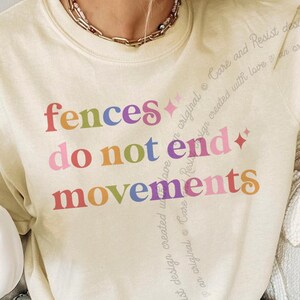 May include: A cream-coloured short-sleeve t-shirt featuring the text "fences do not end movements" printed in a multi-coloured gradient font. The design includes small four-pointed star icons and subtle diagonal text accents in a light script font.