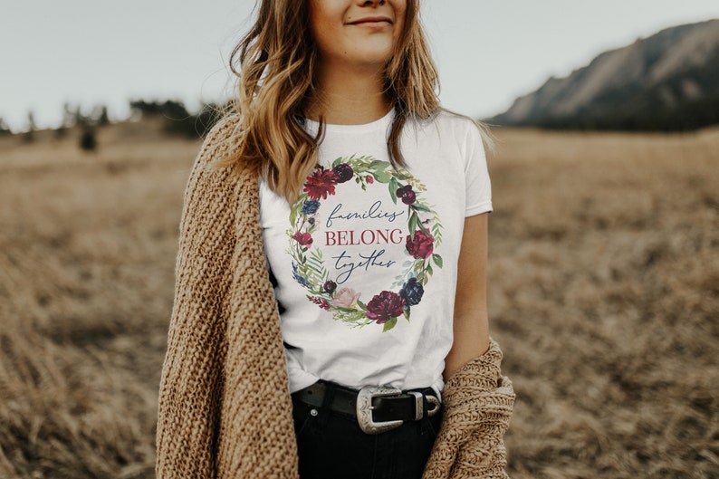 May include: White t-shirt with a floral wreath design and the text "families belong together".