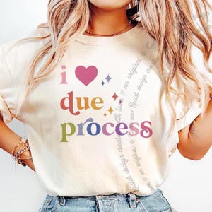 May include: Cream-colored sweatshirt with the phrase "i due process" in colorful letters and a pink heart. The design includes small star and diamond accents. The shirt is a casual, everyday wear item.