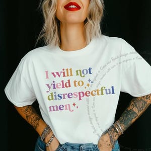 Può includere: T-shirt bianca con la scritta multicolore "I will not yield to disrespectful men". La maglietta ha maniche corte e scollo tondo. Il design include delle stelle.