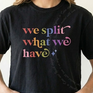 May include: A black short-sleeved t-shirt featuring the text "we split what we have" printed in a multi-colored gradient font. The letters transition through shades of red, orange, yellow, blue, and purple, accompanied by two small star icons.