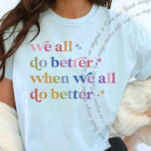 Op de afbeelding: Lichtblauw T-shirt met de tekst "We all do better when we all do better" in kleurrijke letters. Het shirt heeft een ronde hals en korte mouwen. Het ontwerp bevat kleine steraccenten.