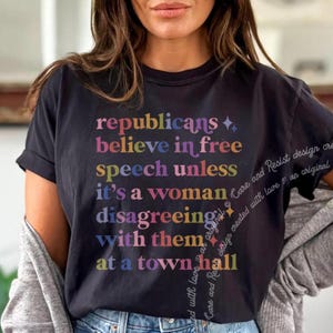 May include: Black t-shirt with a rainbow-coloured text design that reads "republicans believe in free speech unless it's a woman disagreeing with them at a town hall".