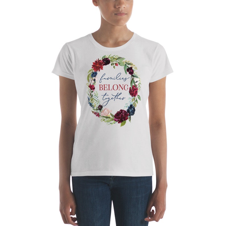 May include: White t-shirt with a floral wreath design and the text "families belong together" in blue and red lettering.