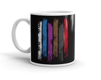 Puede incluir: Taza de café de cerámica blanca con fondo negro y cinco rayas verticales de diferentes colores, que representan los diferentes rangos de cinturón en Jiu-Jitsu brasileño.
