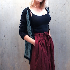 Könnte beinhalten: Eine Frau trägt einen schwarzen und grünen Cardigan über einem schwarzen Tanktop und einem burgunderfarbenen Rock.