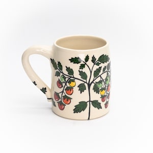 May include: A white ceramic mug with a green, red, and yellow tomato plant design. The mug has a handle and is perfect for enjoying your favorite beverage.