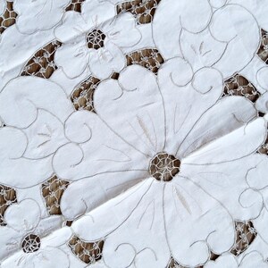 May include: White cotton tablecloth with intricate embroidered floral designs. The tablecloth features a delicate lace pattern and a raised, textured floral motif.