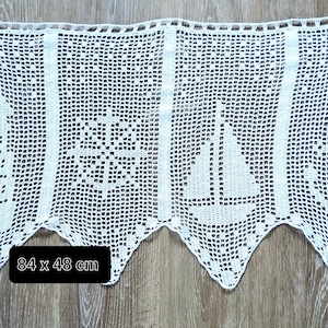 May include: White, crocheted nautical-themed valance featuring a lighthouse, ship's wheel, sailboat, and anchor design. The valance measures 33 x 19 inches. The bottom edge has a scalloped design. The valance is displayed on a wooden surface.