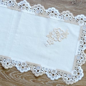 Può includere: Tovaglia da tavolo bianca con un delicato bordo in pizzo e un motivo floreale beige. Il pizzo è una combinazione di bianco e beige.