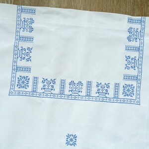 Puede incluir: Tela blanca con un dise&ntilde;o floral bordado en azul. El dise&ntilde;o incluye bordes y patrones de esquina con motivos florales. La tela es probablemente un mantel o un textil decorativo.