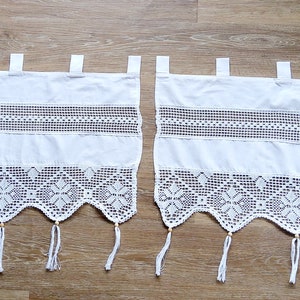 Pode incluir: Duas cortinas brancas de crochê com uma parte inferior ondulada e borlas. As cortinas têm um padrão de renda delicado e são perfeitas para adicionar um toque de elegância a qualquer janela.