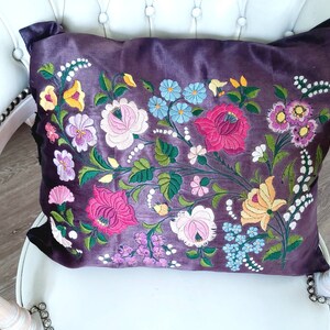 Peut inclure: Un coussin en velours violet avec des motifs floraux brodés dans des tons de rose, jaune, bleu et vert.