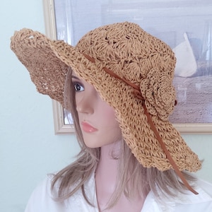 May include: A wide-brimmed straw hat with a crocheted design and a brown leather ribbon tied around the crown. The hat has a flower accent on the side.