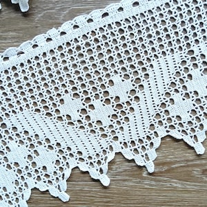 May include: White crocheted lace trim with a delicate floral pattern. The lace has a scalloped edge and is perfect for adding a touch of elegance to any project.