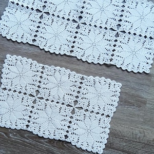 Peut inclure: Deux napperons en crochet blanc avec un motif floral. Les napperons sont de forme carrée et ont un design délicat en dentelle.