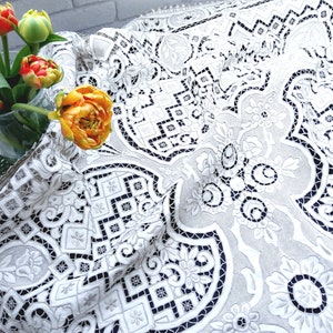 May include: White lace tablecloth with a delicate floral pattern and intricate geometric designs. The tablecloth is made of fine, lightweight fabric and has a soft, flowing texture.
