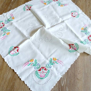 May include: White tablecloth with a scalloped edge and embroidered floral designs in red, pink, yellow, green, and blue.