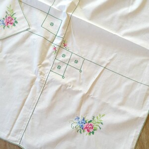 May include: White tablecloth with green embroidered floral designs. The tablecloth has a delicate green border and features a floral pattern with pink, blue, and green flowers.
