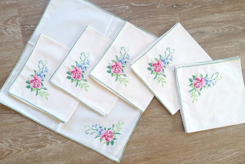 May include: Set of six white linen napkins with green embroidered floral designs featuring pink roses and blue flowers.
