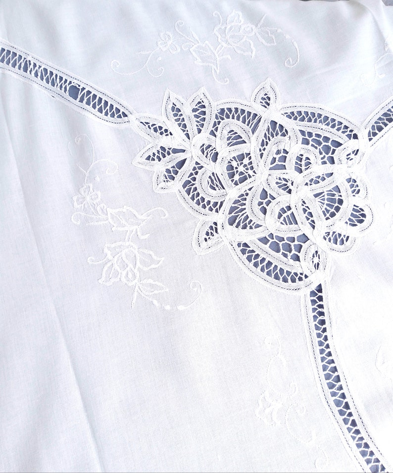 Puede incluir: Tela de algod&oacute;n blanca con delicado bordado de encaje blanco. El encaje presenta un dise&ntilde;o floral con detalles intrincados.