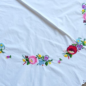Może przedstawiać: Biały okrągły obrus z falbanką i kolorowymi haftowanymi wzorami kwiatowymi.