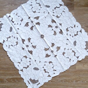 May include: White cotton tablecloth with intricate embroidered floral designs. The tablecloth features a delicate lace pattern and is perfect for adding a touch of elegance to any table setting.