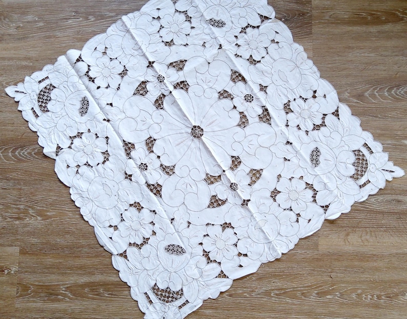 May include: White cotton tablecloth with intricate embroidered floral designs. The tablecloth features a delicate lace pattern and is perfect for adding a touch of elegance to any table setting.