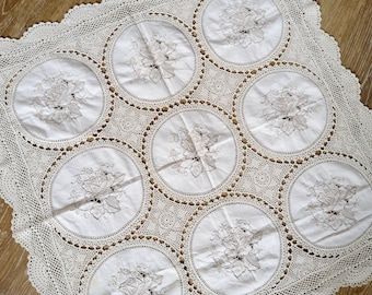 Puede incluir: Un mantel de crochet blanco con un delicado patrón floral. El mantel presenta un diseño repetitivo de motivos circulares con flores bordadas.