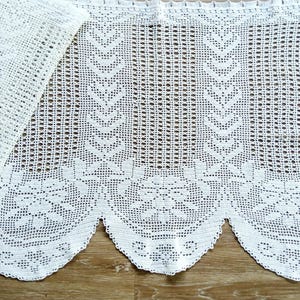 Puede incluir: Primer plano de una cortina de encaje blanco, hecha a ganchillo, con borde festoneado. El intrincado diseño presenta patrones florales y geométricos. La cortina está hecha de una tela delicada de tejido abierto, ideal para la decoración del hogar.