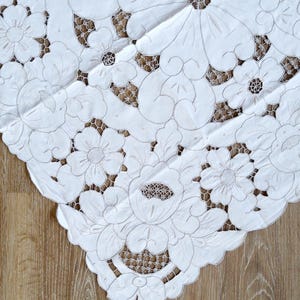 May include: White cotton tablecloth with intricate embroidered floral designs. The tablecloth features a delicate lace pattern and is perfect for adding a touch of elegance to any table setting.