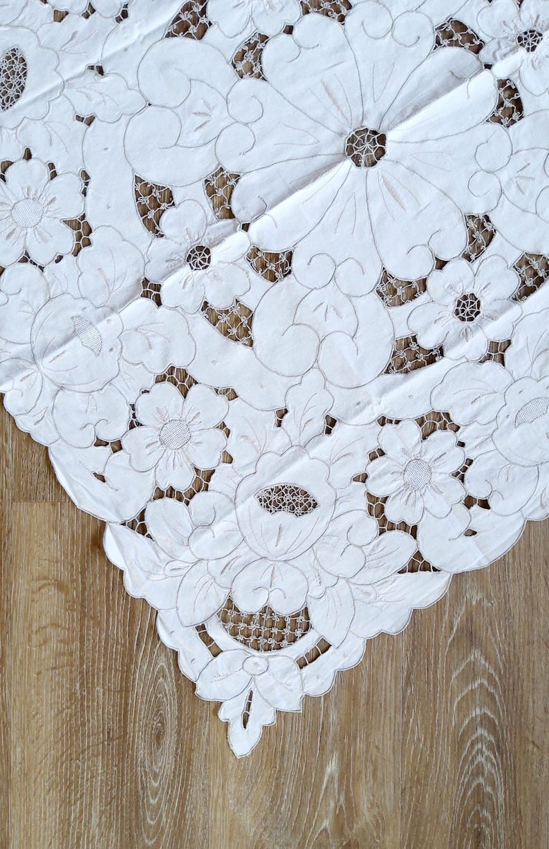May include: White cotton tablecloth with intricate embroidered floral designs. The tablecloth features a delicate lace pattern and is perfect for adding a touch of elegance to any table setting.