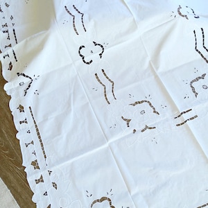 May include: White cotton tablecloth with a delicate floral embroidery design. The tablecloth features a scalloped edge and intricate floral patterns.