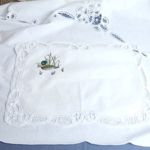 Puede incluir: Mantel blanco con un delicado borde de encaje y una imagen bordada de un pato en un estanque. El mantel es perfecto para una cena formal o una ocasi&oacute;n especial.