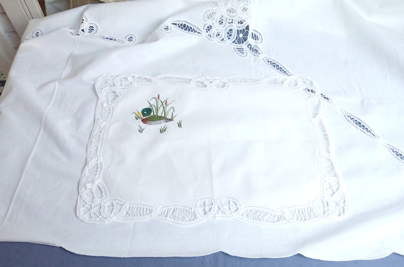 Puede incluir: Mantel blanco con un delicado borde de encaje y una imagen bordada de un pato en un estanque. El mantel es perfecto para una cena formal o una ocasi&oacute;n especial.