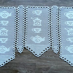 Puede incluir: Cortina de ganchillo blanca con un patrón repetido de teteras y tazas. El delicado diseño de encaje está enmarcado por un borde festoneado. Esta decoración de cocina hecha a mano añade un toque de encanto vintage.