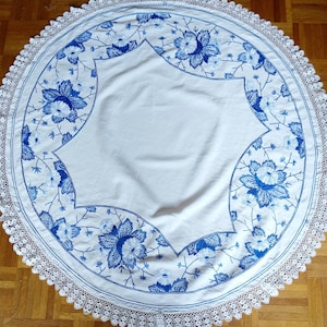 May include: A white tablecloth with a blue floral embroidery design and a white crocheted lace border.