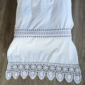 Può includere: Pannello per tende in cotone bianco con un bordo in pizzo all'uncinetto. Il bordo in pizzo presenta un motivo ripetitivo di cerchi e conchiglie.