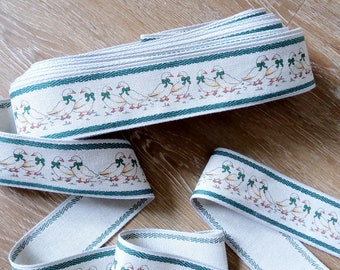 May include: White fabric ribbon with a green border and a repeating pattern of white geese with green bows. The geese are walking in a line.