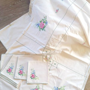 May include: A white tablecloth with green embroidered trim and floral designs. The tablecloth is accompanied by six matching napkins with the same floral design.