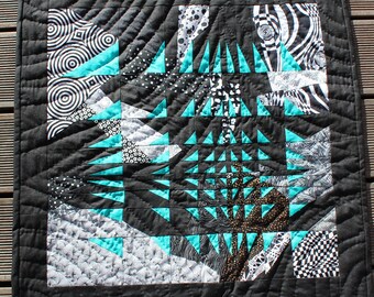 Peut inclure: Une courtepointe noire et blanche avec un motif géométrique de triangles turquoise. La courtepointe est faite de différents tissus avec divers motifs, y compris des cercles, des rayures et des pois.