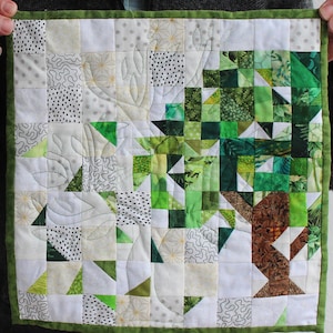 Puede incluir: Una colcha de retazos verde y blanca con un diseño geométrico. La colcha está hecha de varias telas con diferentes patrones, incluyendo lunares, remolinos y hojas. La colcha está bordeada con un borde verde.