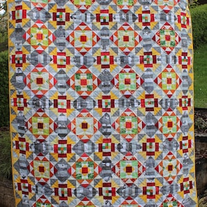 Könnte beinhalten: Eine Quiltdecke mit einem geometrischen Muster aus Quadraten, Dreiecken und Rauten in Rot-, Gelb-, Grün- und Grautönen.